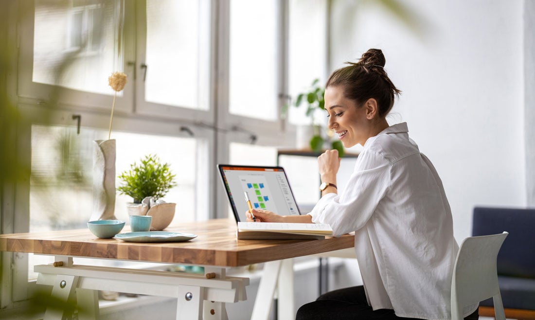 Smiling professional working on a laptop at a bright, modern desk, reviewing colorful charts – illustrating how quality management tools support effective and organized workflows.